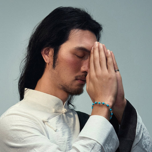 A man meditating while wearing a Tibetan turquoise meditation bracelet, using emotional healing stones for inner peace.