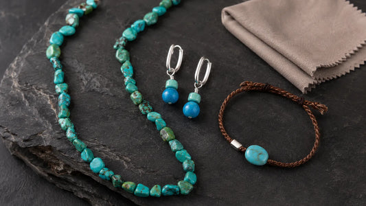 Turquoise necklace, silver drop earrings, and braided bracelet arranged on dark stone beside a jewelry cleaning cloth.