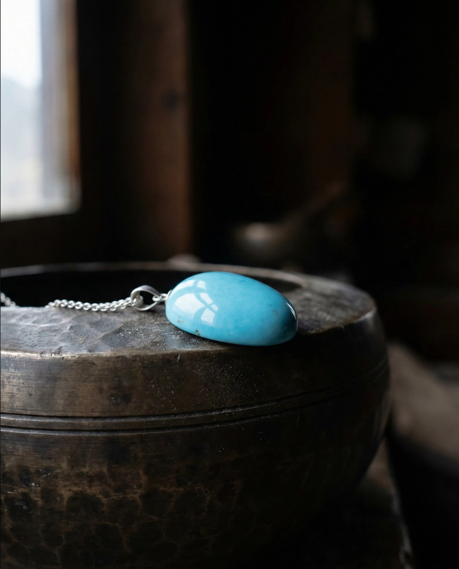 A smooth, calming Tibetan turquoise stone resting on a rustic wooden barrel by soft natural window light, representing the Serenity Collection.