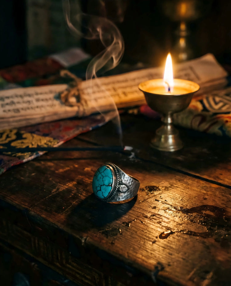 An authentic Tibetan turquoise ring sitting on a vintage wooden desk beside a glowing candle and old manuscript, representing the Wisdom Collection.