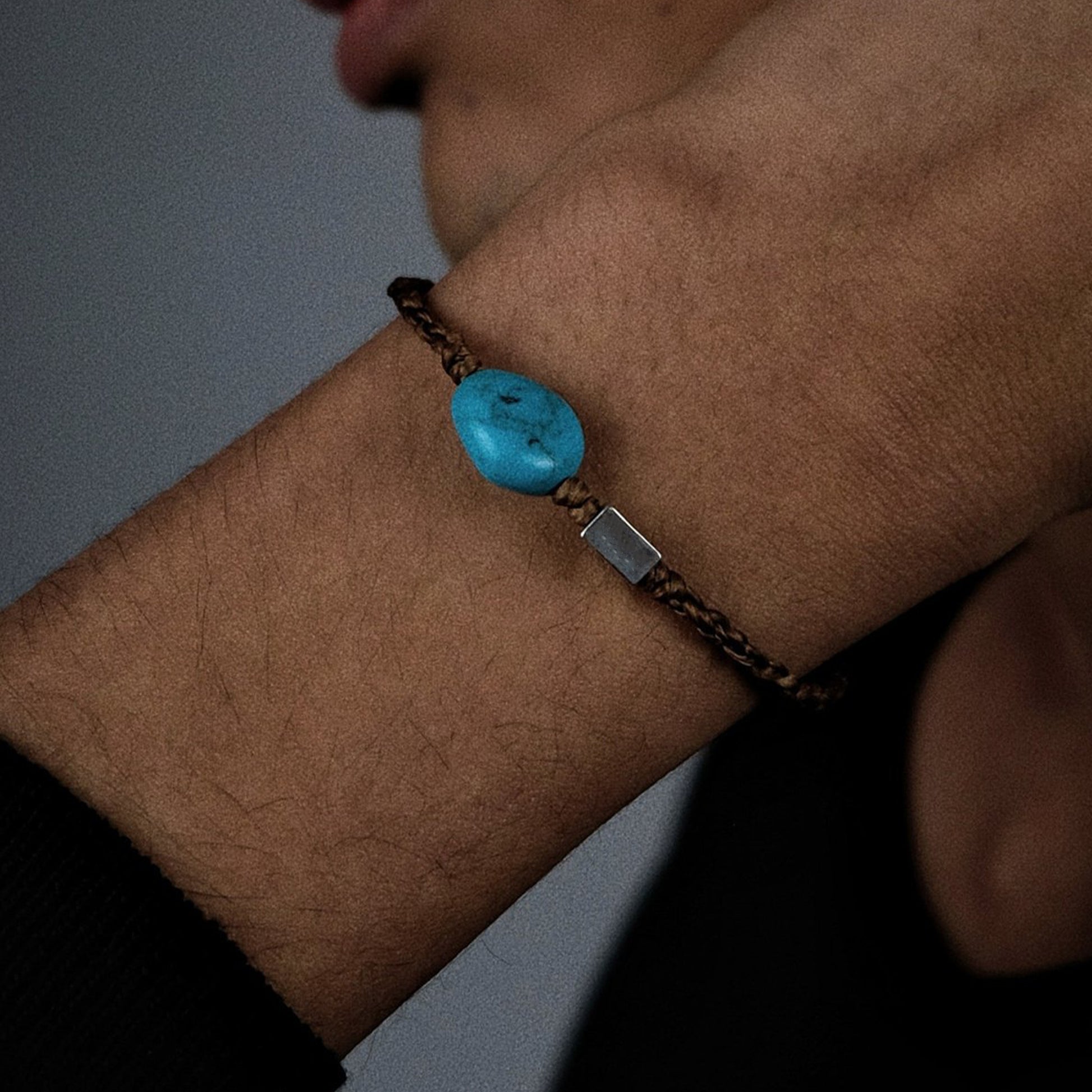 Extreme close-up of the smooth Tibetan turquoise and the masterful braiding of the earth-toned cord.