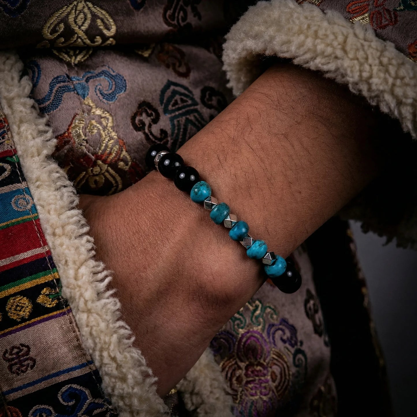 A model wearing the Eclipse Tibetan turquoise bracelet, showcasing its contrast against dark textures.