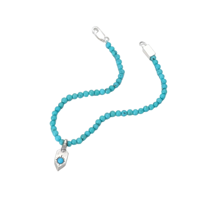 Angled view of the fluid turquoise bead bracelet and the hand-stamped silver shield charm.