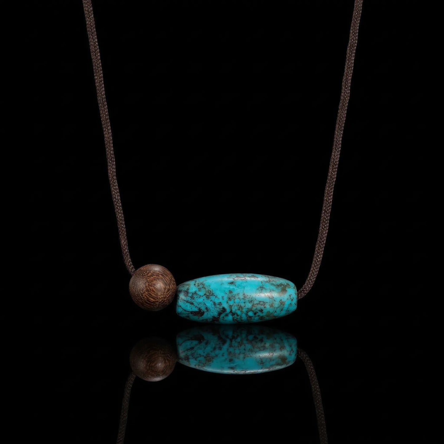 The Grounded Spirit Necklace featuring a barrel-cut Tibetan turquoise and a single wood bead on a dark background.