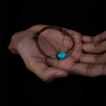 The Anchor Bracelet resting in an open palm, showcasing its tactile hand-braided cord and blue stone.