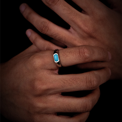 Perspective view of the elongated turquoise ring on a finger against a dark background.