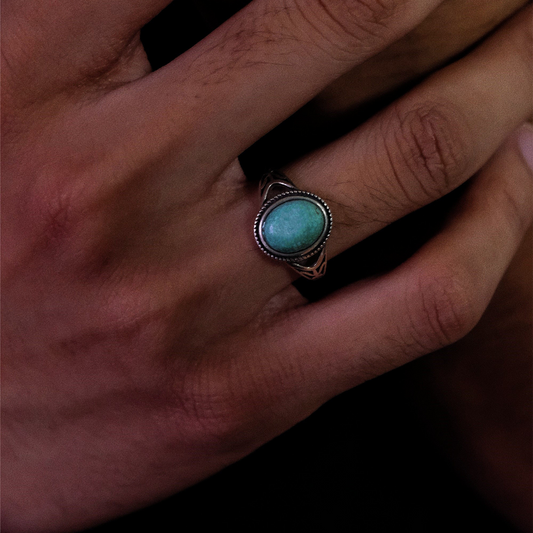 Close-up of a model's hand wearing the Nomad's Shield turquoise ring against a dark background.