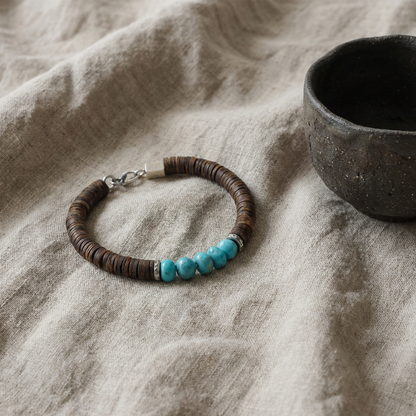 The Grounding Bracelet displayed on a neutral linen surface next to a dark tea bowl, reflecting ritual and heritage.
