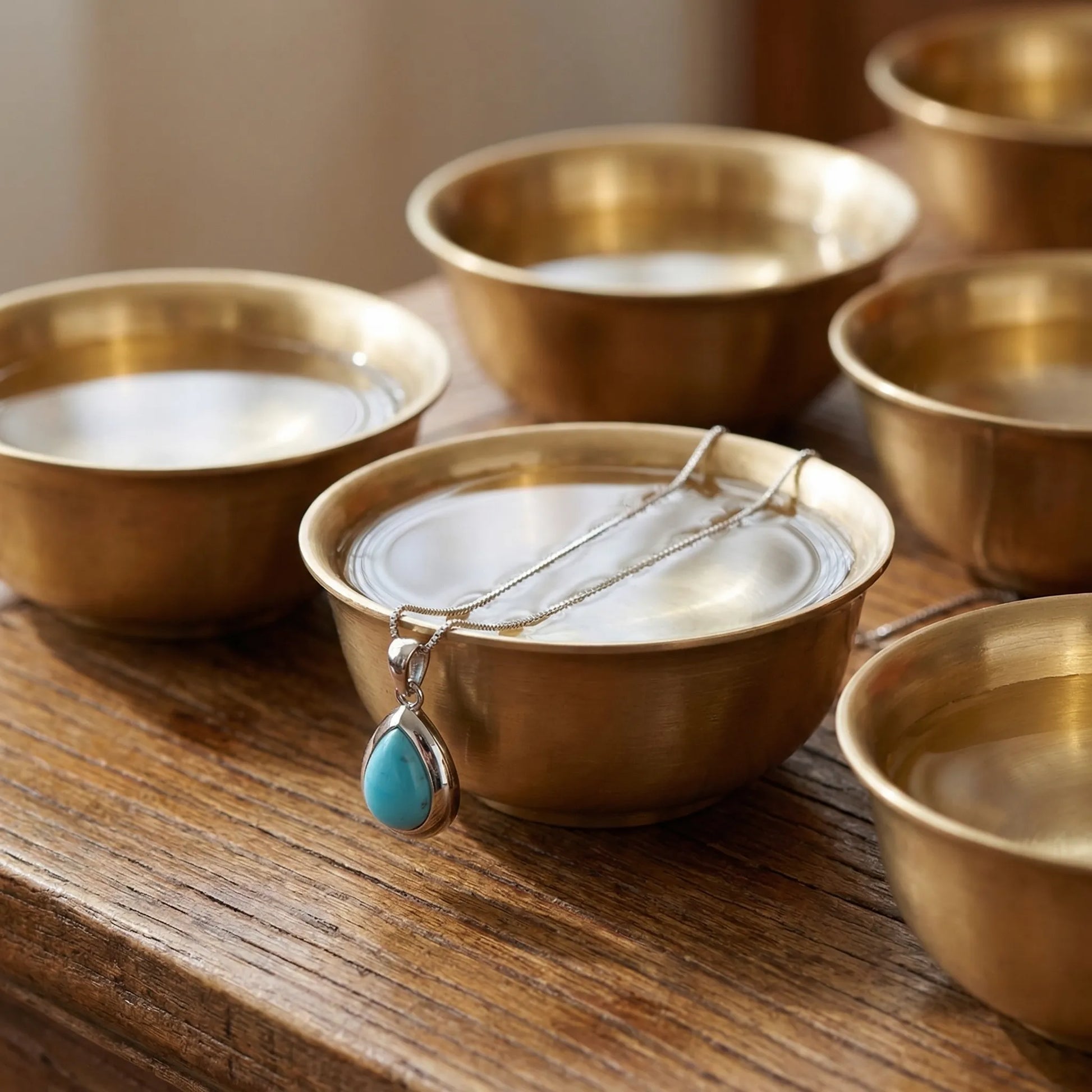 The Pure Drop necklace displayed with traditional Tibetan brass bowls, symbolizing purity and clarity.