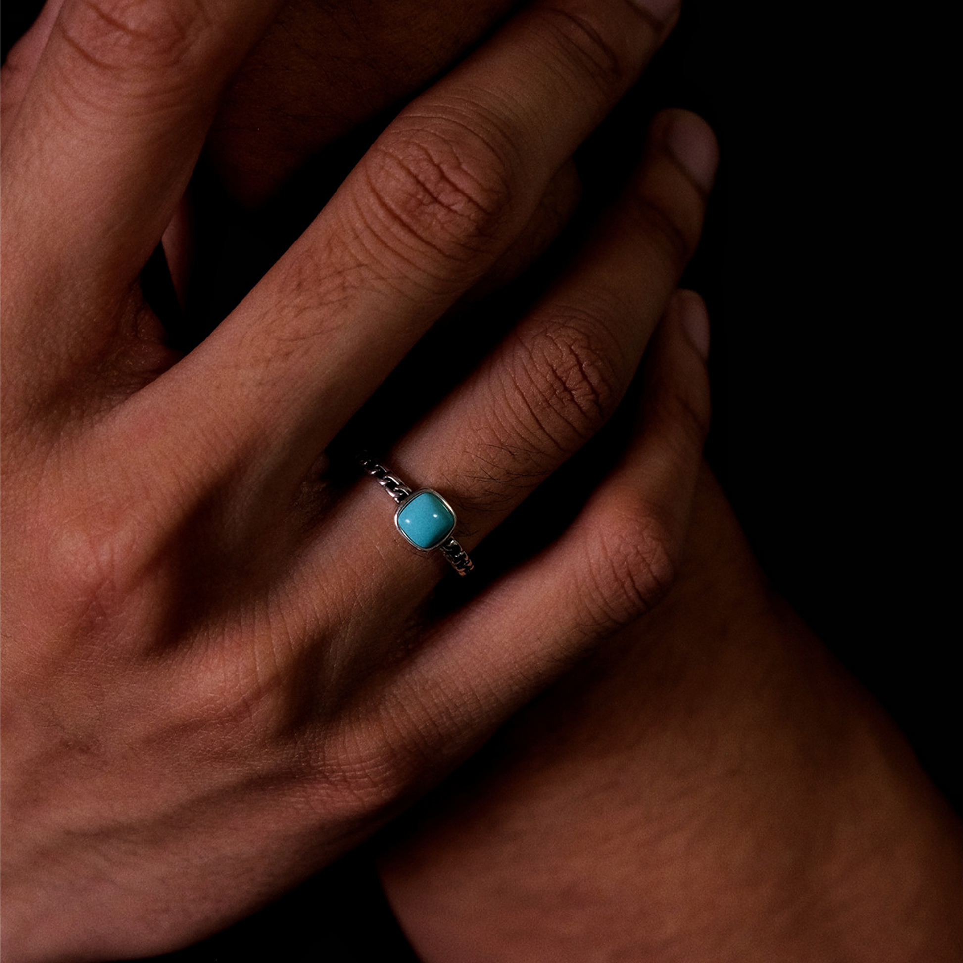 Perspective view of the cushion-cut turquoise chain ring on a finger against a dark background.