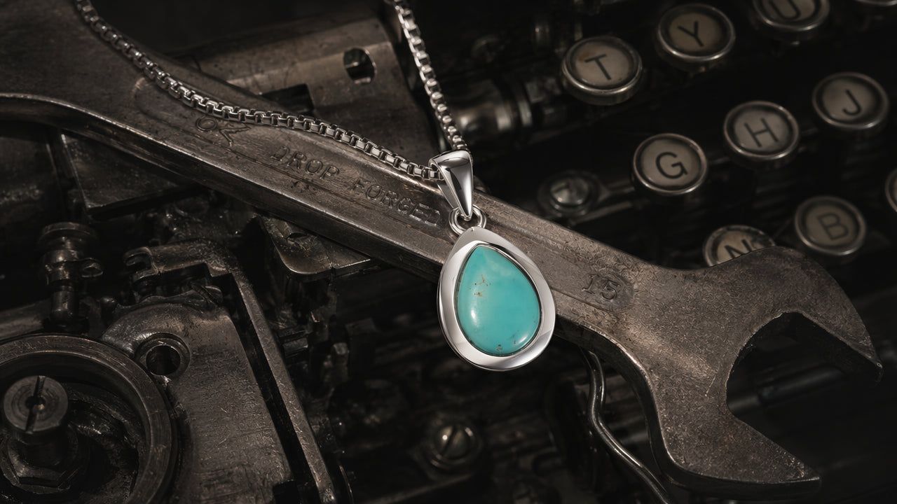 A raw turquoise necklace for men draped elegantly over a heavy vintage metal wrench, illustrating how a men's healing crystal necklace complements a rugged, quiet luxury aesthetic.