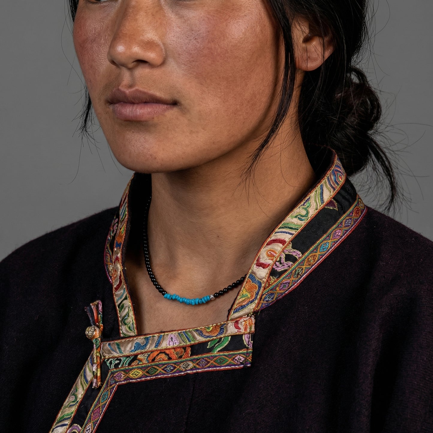 Portrait of a woman wearing the Tibetan turquoise and onyx healing necklace in a traditional setting.